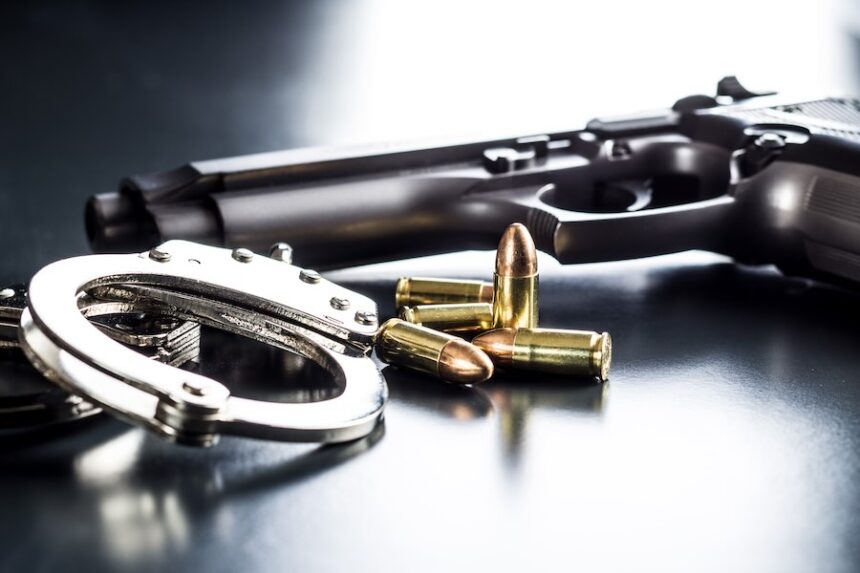 Pistol bullets, handgun and handcuffs on black table.