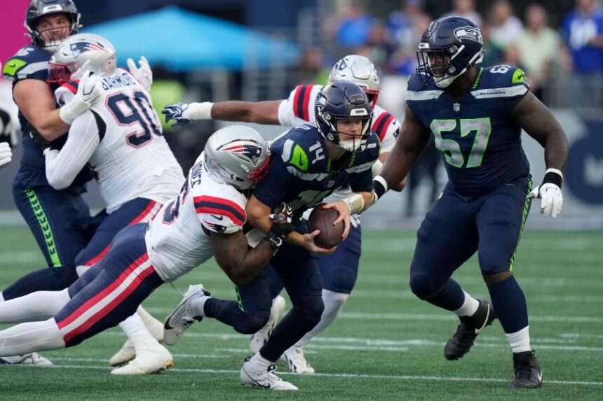 Seattle Seahawks quarterback Sam Darnold, center, is sacked by New England Patriots linebacker Dre'mont Jones, left, as Seattle Seahawks linebacker Connor O'Toole is at right, during the first half of an NFL football game, Wednesday, Sept. 9, 2026, in Seattle. (AP Photo/Stephen Brashear)