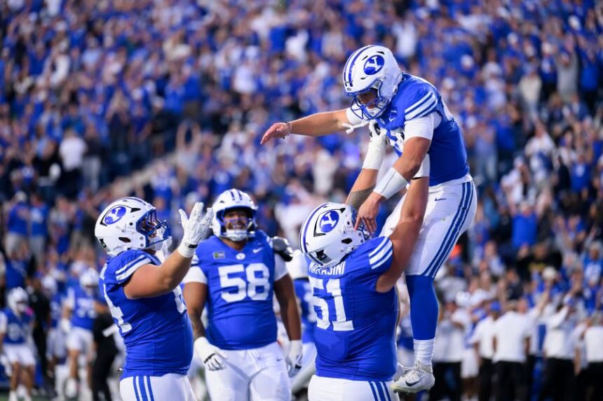 BYU offensive lineman Sonny Makasini, center right, lifts quarterback Bear Bachmeier, top, after Bachmeier ran for a touchdown during the first half of an NCAA college football game against Notre Dame, Saturday, Oct. 17, 2026, in Provo, Utah. (AP Photo/Tyler Tate)