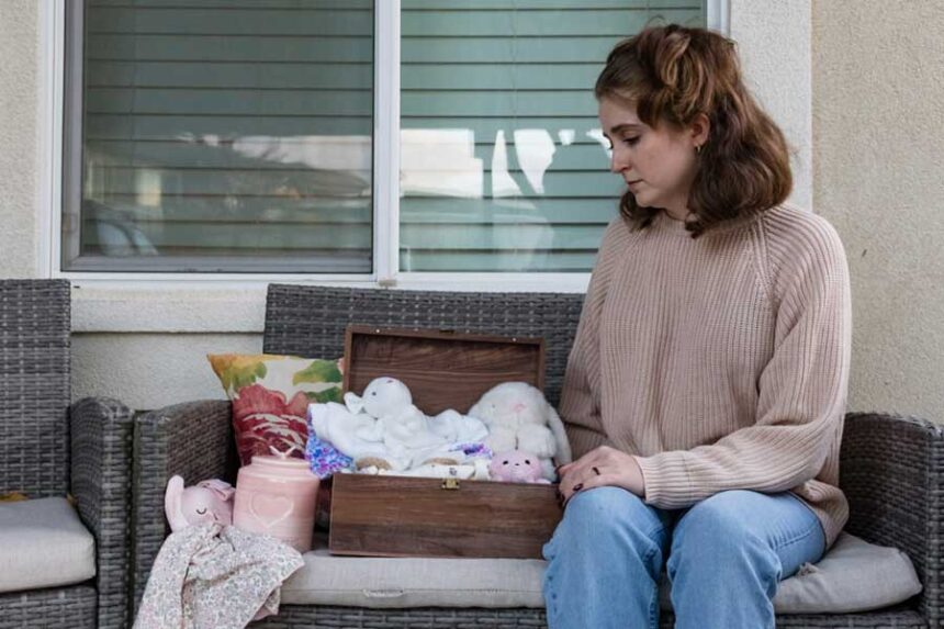 Rebecca Crozier, 27, of Meridian, Idaho, poses in October 2026 with mementos from her baby, Haven. At 11 weeks, she received a fatal fetal diagnosis of anencephaly, and had to travel out of state to terminate the pregnancy because of her state’s near-total abortion ban. (Photo by Otto Kitsinger for Stateline)