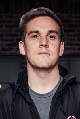 Tyler TeeP standing in front of dark brick wall in black jacket