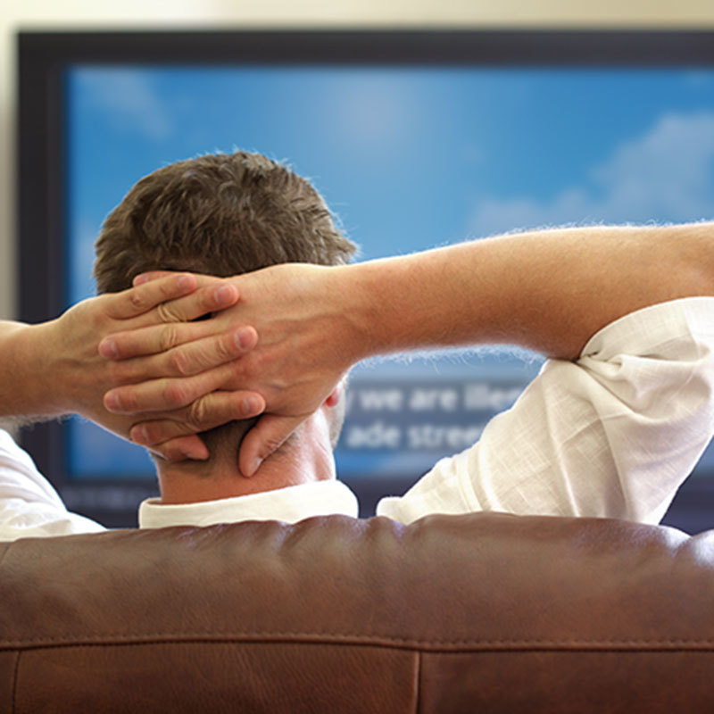 man putting his hands behind his head while watching TV