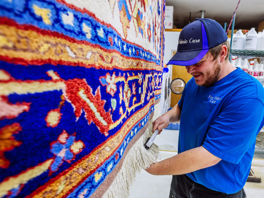 fine fabric care employee brushing carpet fringe as last step to carpet cleaning