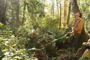 Teenage boy leaning against tree in sunny forest