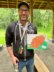 Smiling man holding pastel drawing of pinecone in nature pavilion.