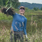 Young woman in grassy wetlands hoisting mass of dirt and plants