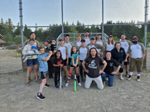 Group shot of adults and kids on a sandy baseball field.