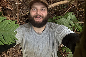 Selfie of young bearded man in baseball cap on forest floor