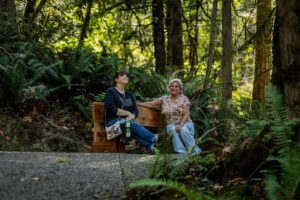 Two women sitting on bench in forest.