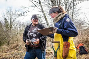 Young man and woman looking at clipboard near trees