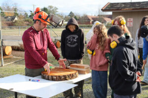 Man showing students 2x4 lumber and a cut timber round.
