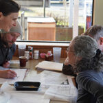Photo of four people sitting at a table with drawings at a cafe.