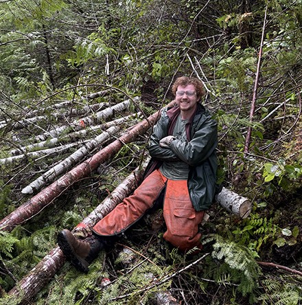 Photo of a man sitting among cut logs.