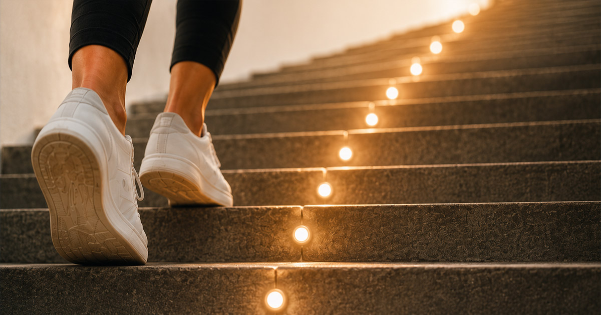 Close-up of a person in sneakers walking up stone stairs lined with glowing lights, symbolizing small incremental progress toward health goals.