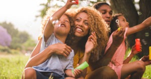 Young african-american family sharing a special moment in the sun blowing colouful soap bubbles and laughing toghether cheerfully.