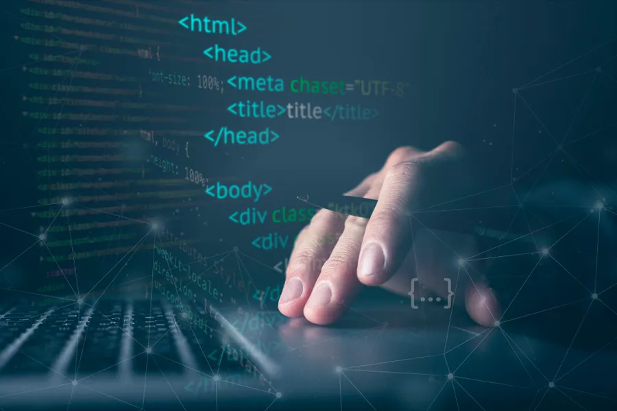 Hand holding a pen touching a laptop touchpad with html codes as foreground