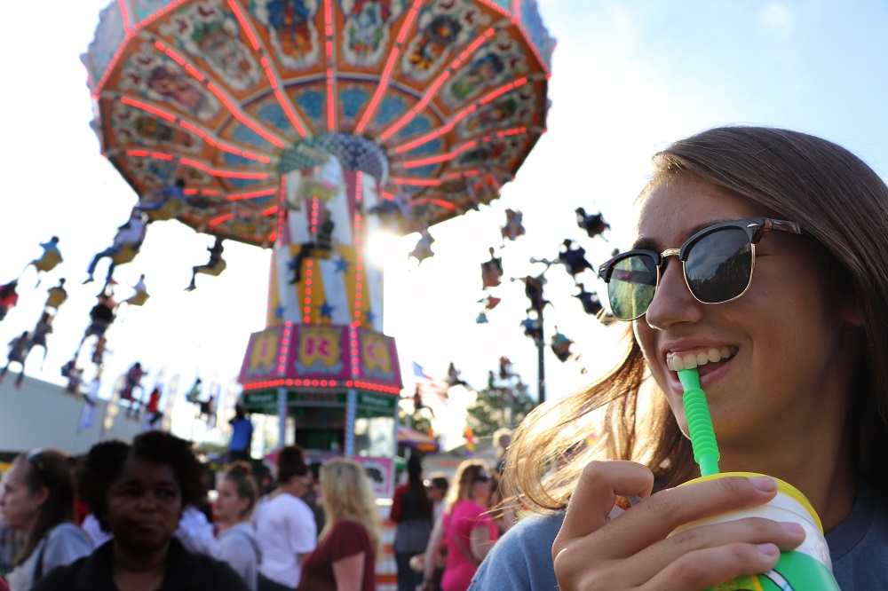 Fair scene with young woman sipping drink.