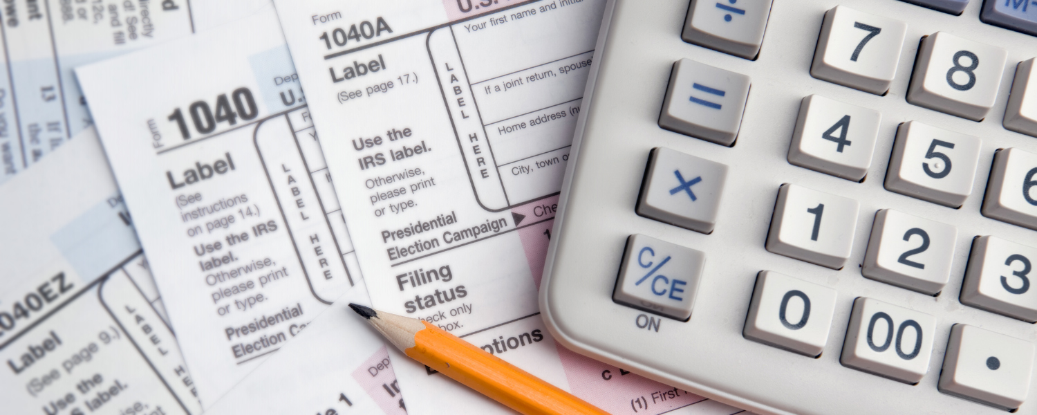 many 1040 tax forms spread on a desk with a pencil and a calculator