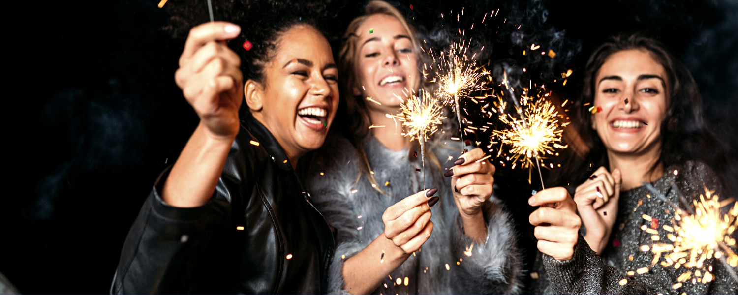 photograph of three young women laughing and holding sparklers