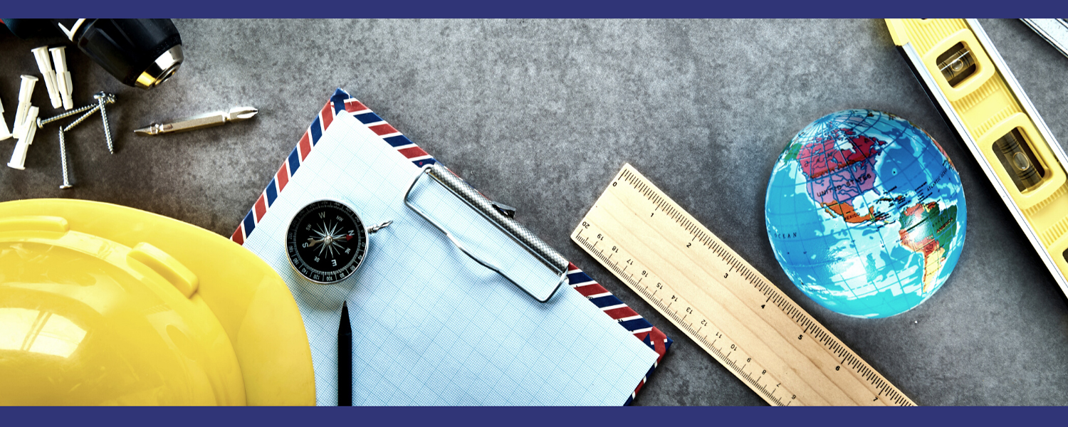 photograph of a table with a power drill, hard hat, clip board, ruler, globe, and level