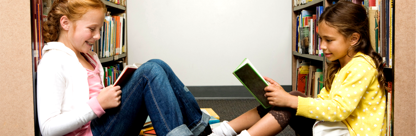 two young girls sitting on the floor in the stacks reading books