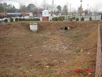 Detention pond with unwanted vegetation. Volume capcity could be impacted as well due to trees that are growing in the pond. To many trees and other unwanted vegetation do not allow for the wanted vegetation to grow correctly and can also cause erosion issues. Trees and other woody vegetation damage the structures in the pond if left unmaintained.