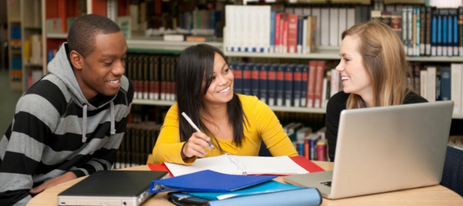 three young adults with notebooks working on a laptop in the library