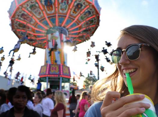 Fair scene with young woman sipping drink.