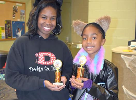Photo of 2 girls holding a trophy and dressed for Halloween.