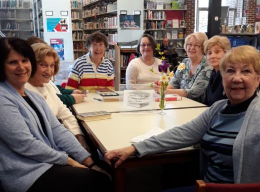 many smiling women sitting around a table with books