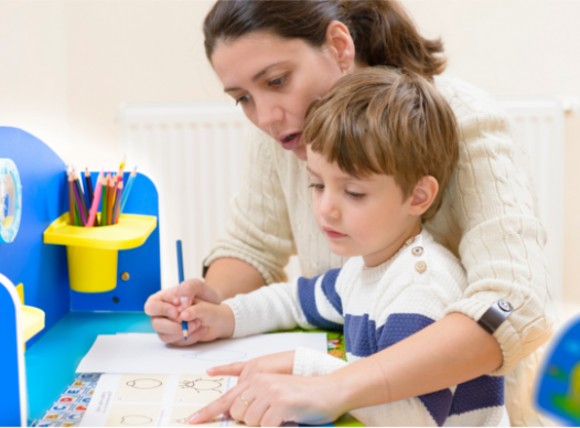 a mother helping a child write while sitting at a desk together