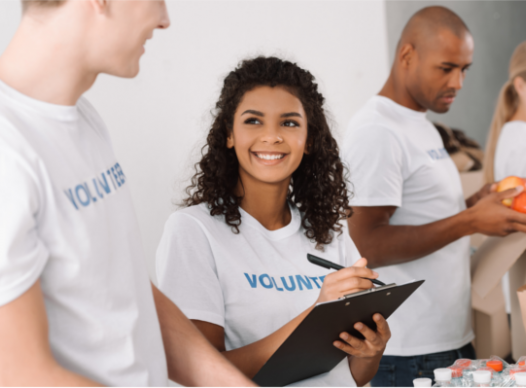 young woman smiling, holding a clipboard, and wearing a 'volunteer' shirt
