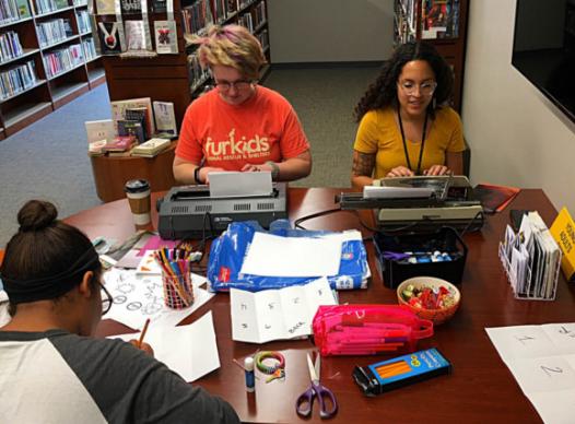 teens working on zines at a desk cluttered with crafting supplies