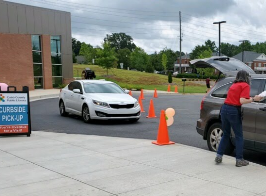 library staff member delivers bag of books to patron's car while another car waits in line