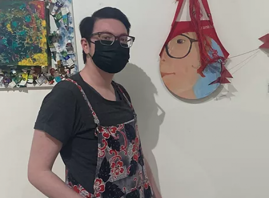 Man with brown hair, glasses and mask standing in front of art work