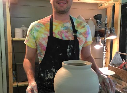 Man with glasses standing behind pottery wheel with large vase