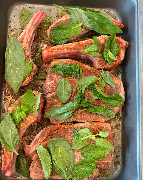 lamb placed into a baking pan with mint leaves and seasonings on top