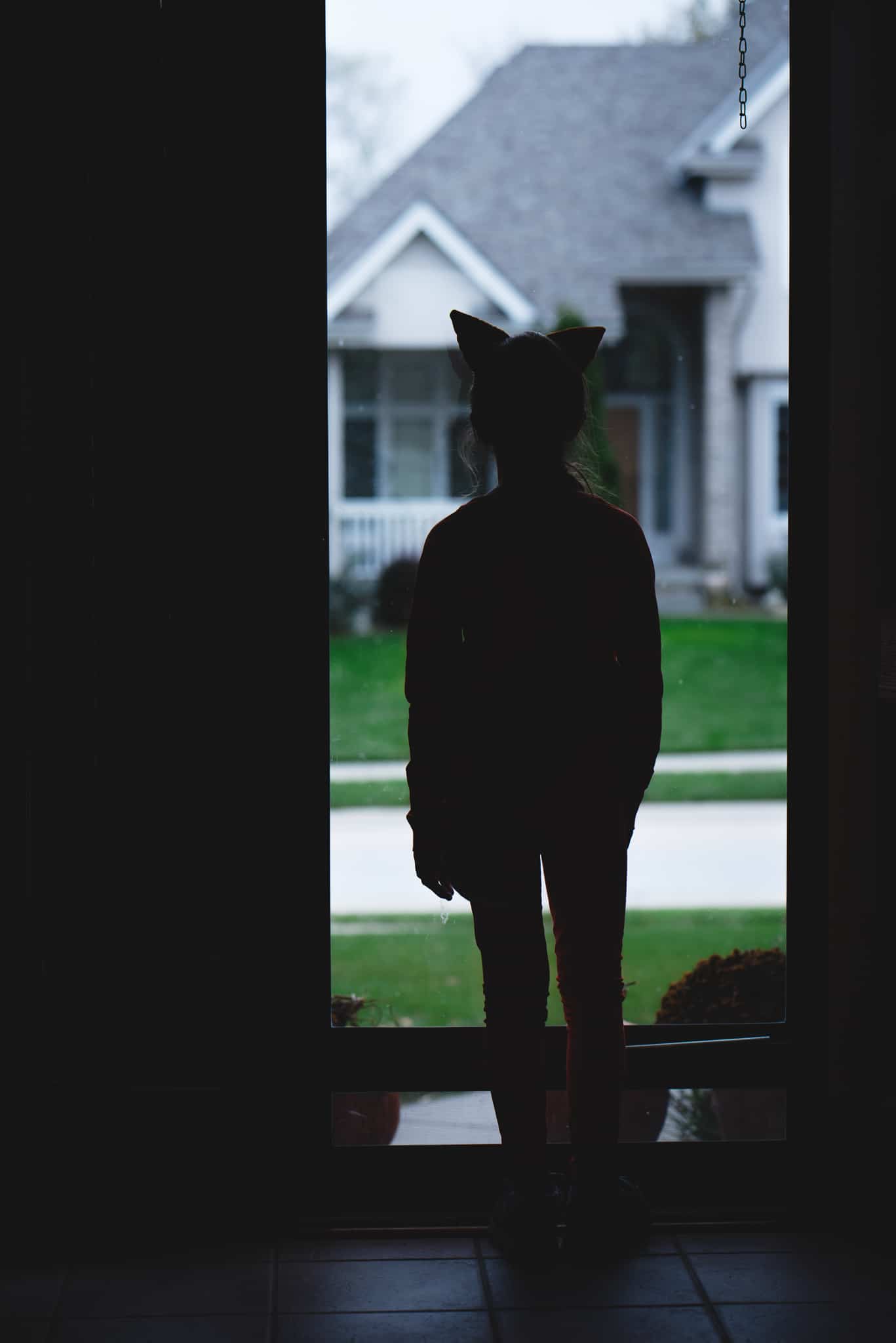 Child in fox costume standing in front of glass door creating a silhouette 
