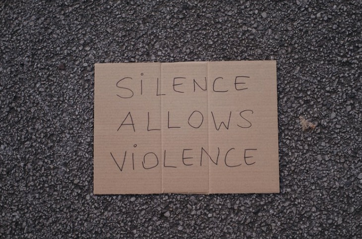 asphalt with cardboard sign that says silence allows violence