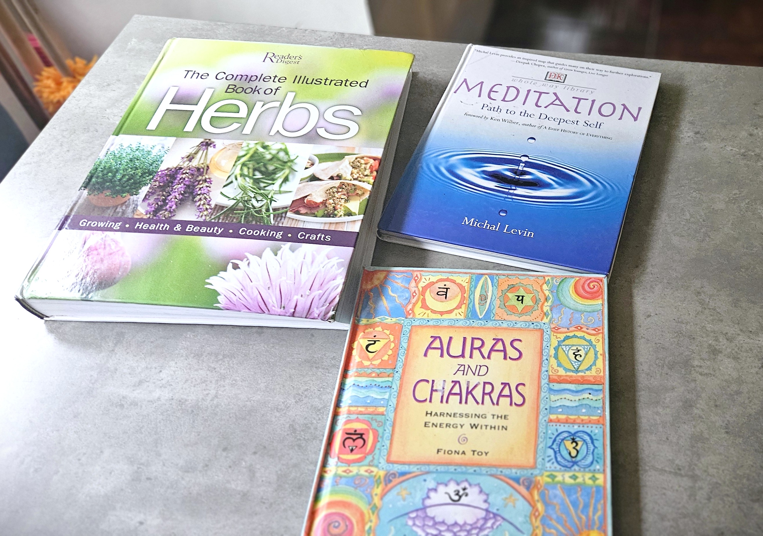 Stack of advanced books on herbs, meditation, and chakras displayed in a home learning space, representing exposure without pressure in unschooling.