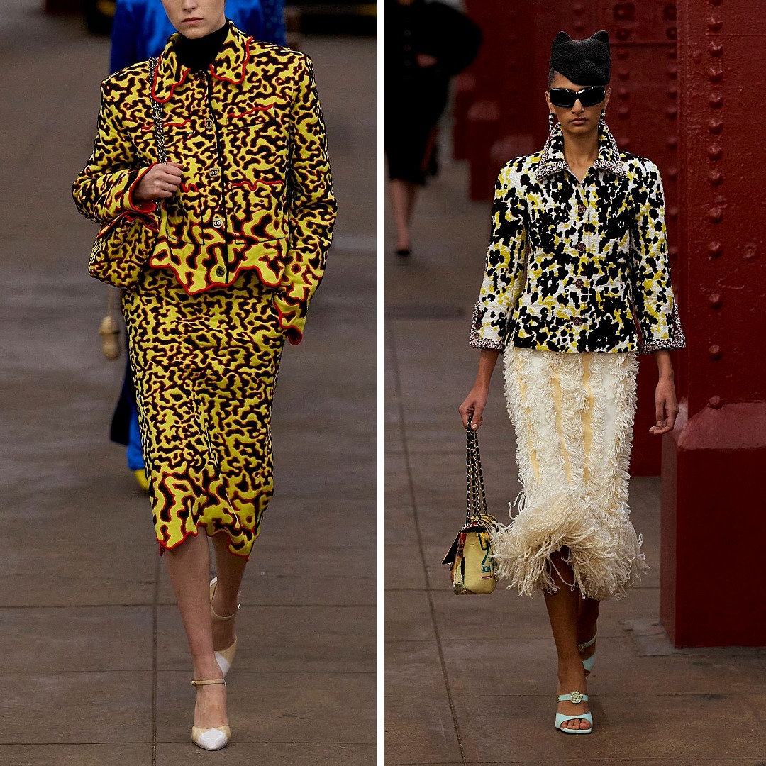 Two runway looks from Chanel Pre-Fall 2026 featuring black-and-yellow palettes. Left: a matching jacket and skirt with an abstract yellow, black, and red textured pattern. Right: a black-and-yellow tweed jacket paired with a cream skirt trimmed with dense feather detailing. Both outfits show Chanel’s latest interpretation of high-contrast colour and surface texture.