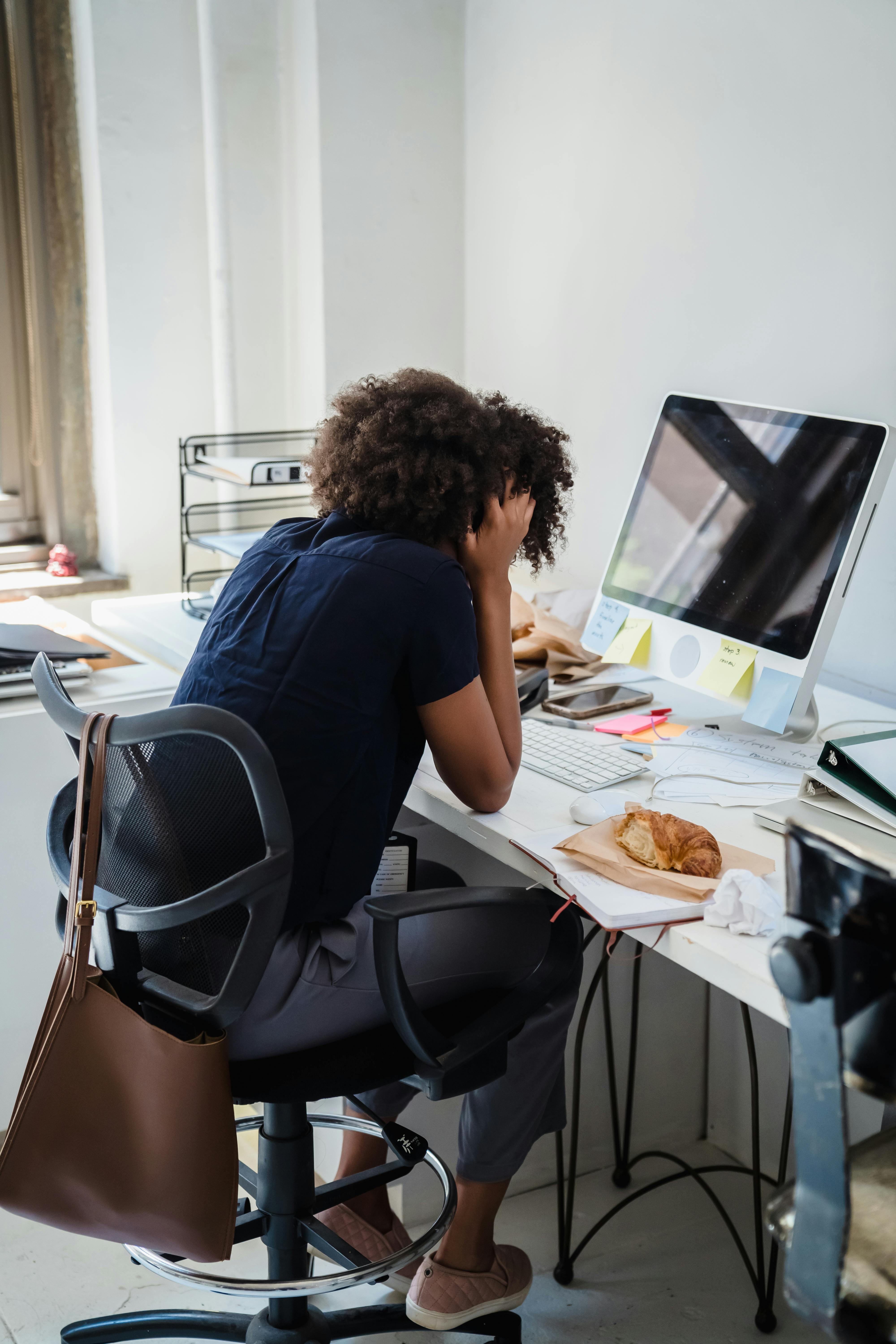 Woman with head in hand appearing overwhelmed at desk, representing PDA anxiety and demand pressure