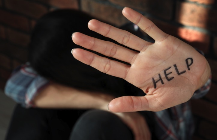 person with their head in their lap with a hand held up that says "help"