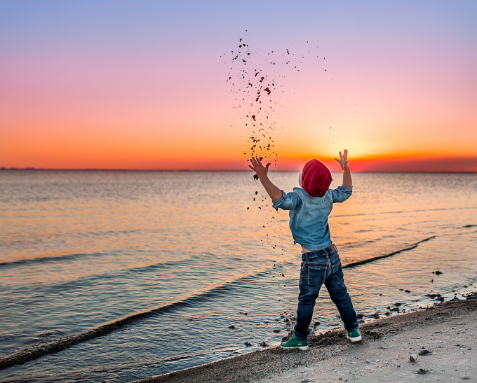 Child throwing sand on beach and freezing the motion