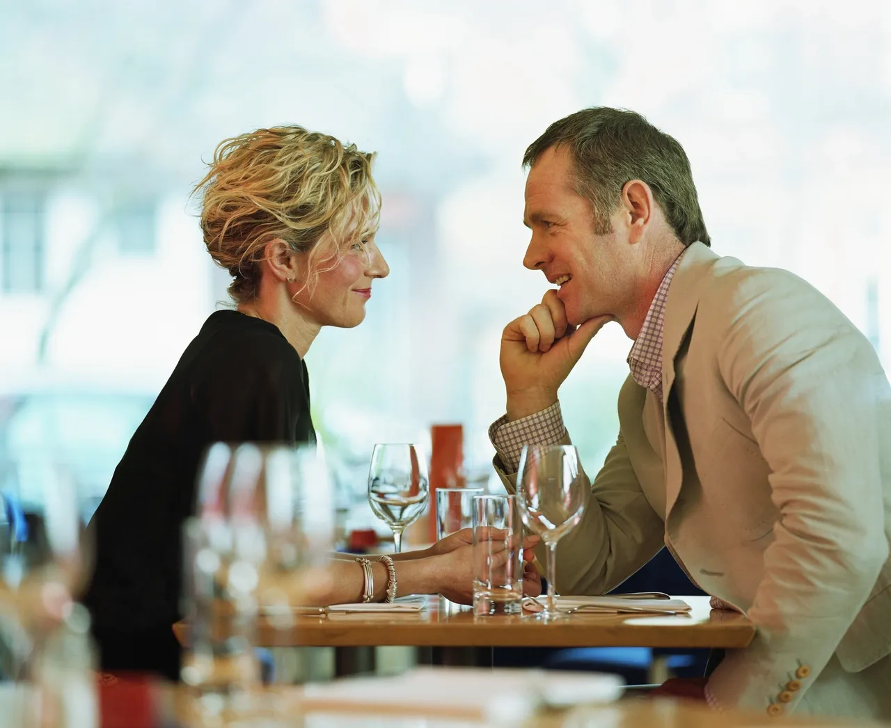 A couple sitting at a restaurant table, smiling and holding hands while engaging in a focused, intimate conversation.
