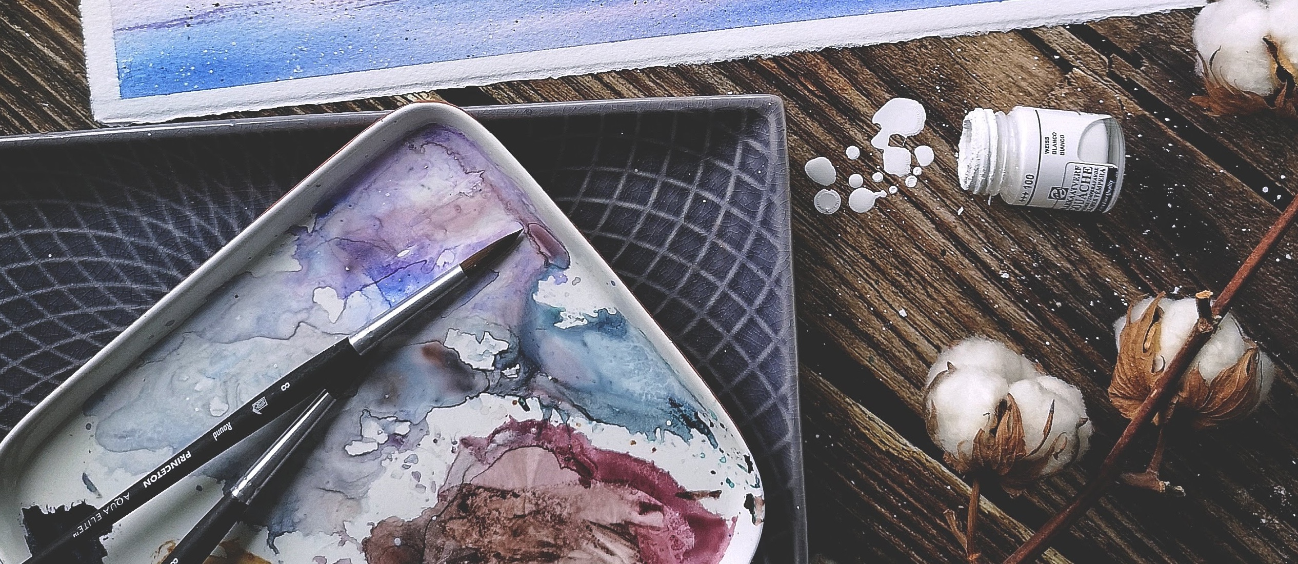 Flatlay of watercolor brushes, paints, and ceramic palette. Spilled Paint on a Wooden Desk