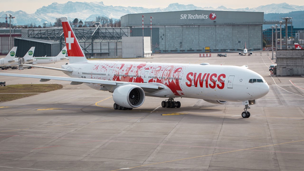 A close-up of Swiss International Airlines' Boeing 777-300ER, featuring the iconic “Faces of Swiss” livery, with portraits of over 2,500 employees from various departments, including cabin crew, pilots, technicians, and support staff, symbolizing a culture of recognition and appreciation within the airline.
