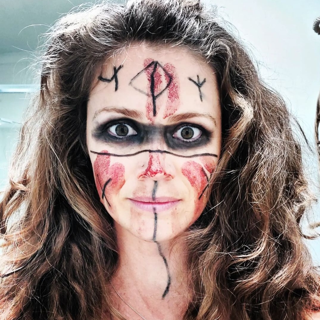 woman face with wild hair eyes wide with fearlessness painted in viking style symbols and blood