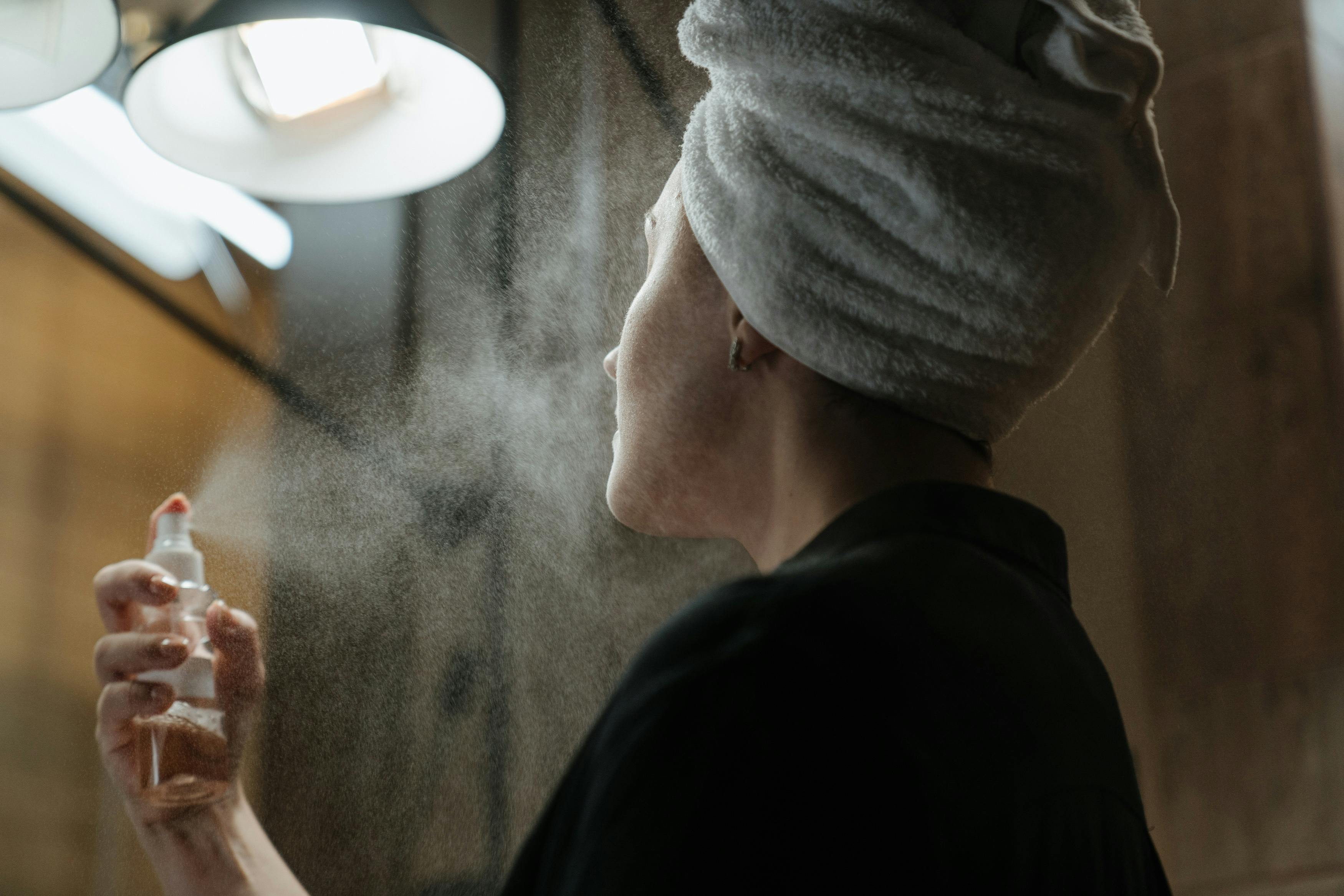 Lady with a towel on her head spritzing her face