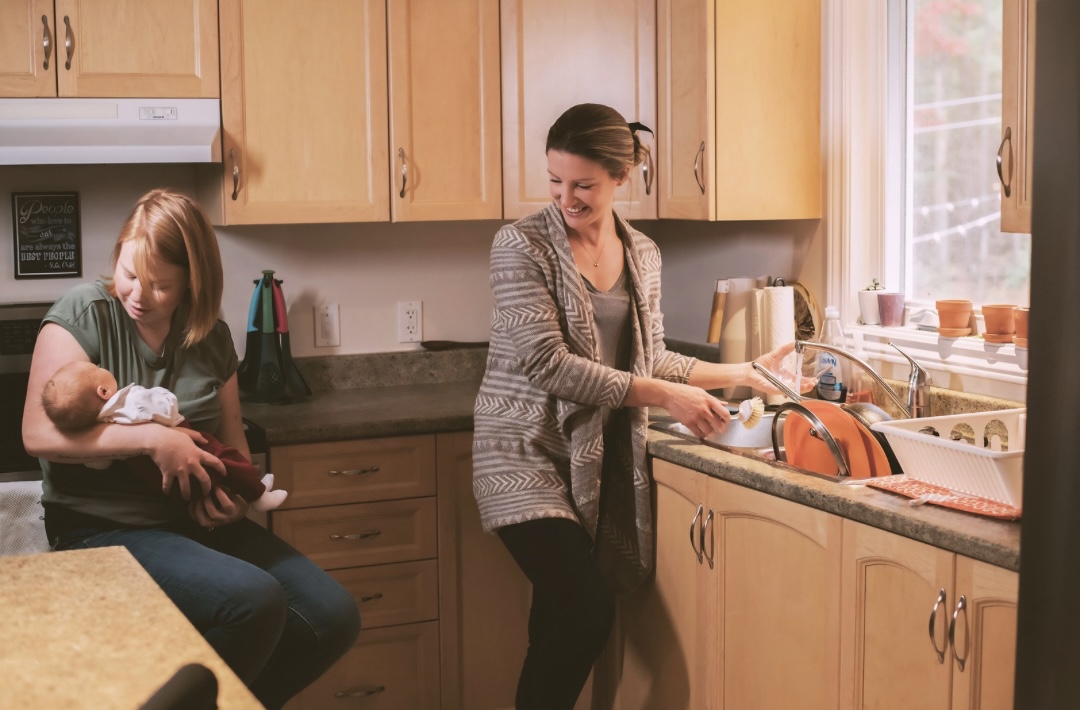 Doula standing in kitchen with a parent holding their baby
